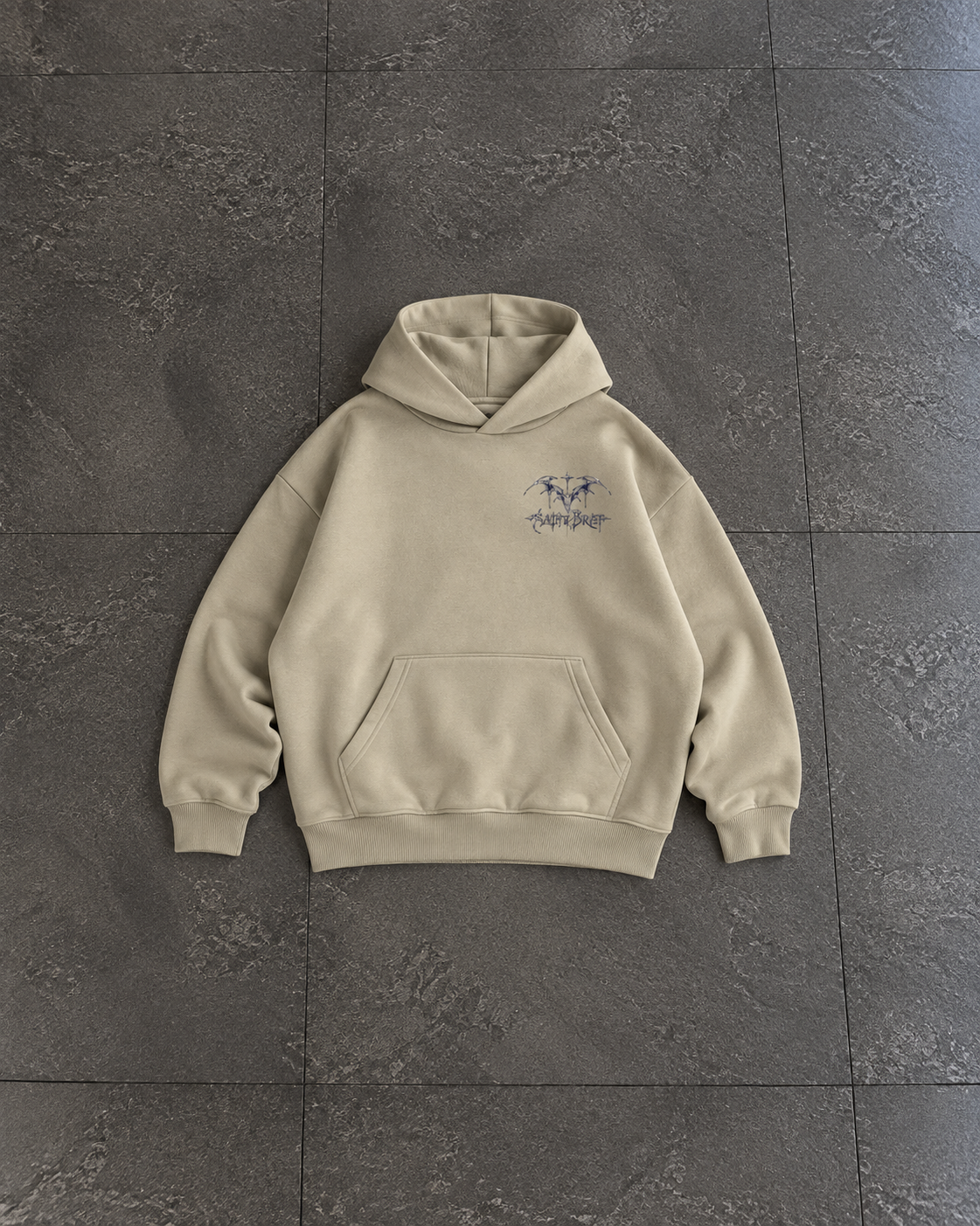 A beige pullover hoodie with a small dark blue graphic on the left chest, laid flat on a dark gray tiled floor.

Color: Stone Front 