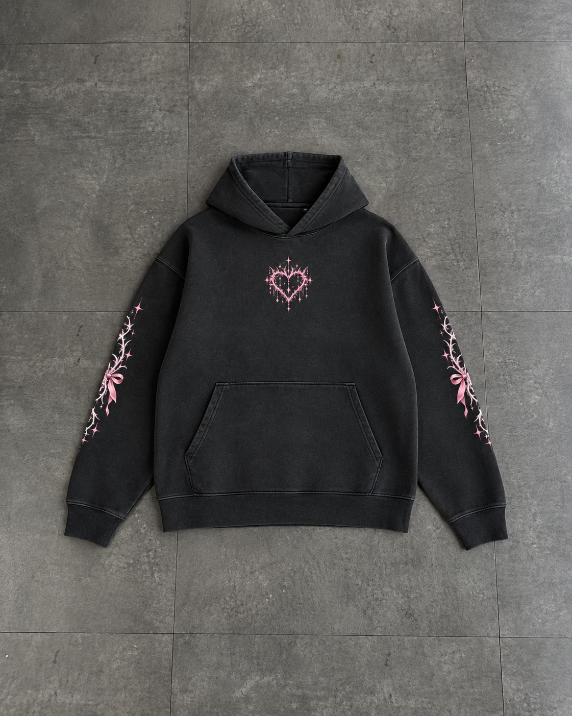 A black washed pullover hoodie with a pink heart design on the chest and pink floral embroidery on both sleeves, laid flat on a gray tiled surface.

Color: Dyed Black Rock Front