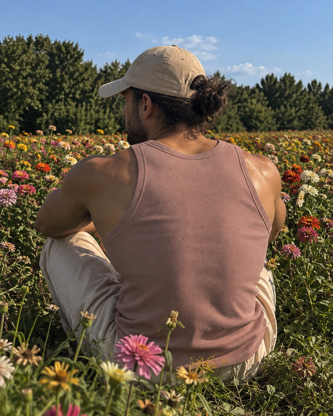 A man wearing a beige baseball cap, a dusty rose tank top, and light beige shorts sits in a field of colorful wildflowers, viewed from behind.

Color: Hazy Pink Back