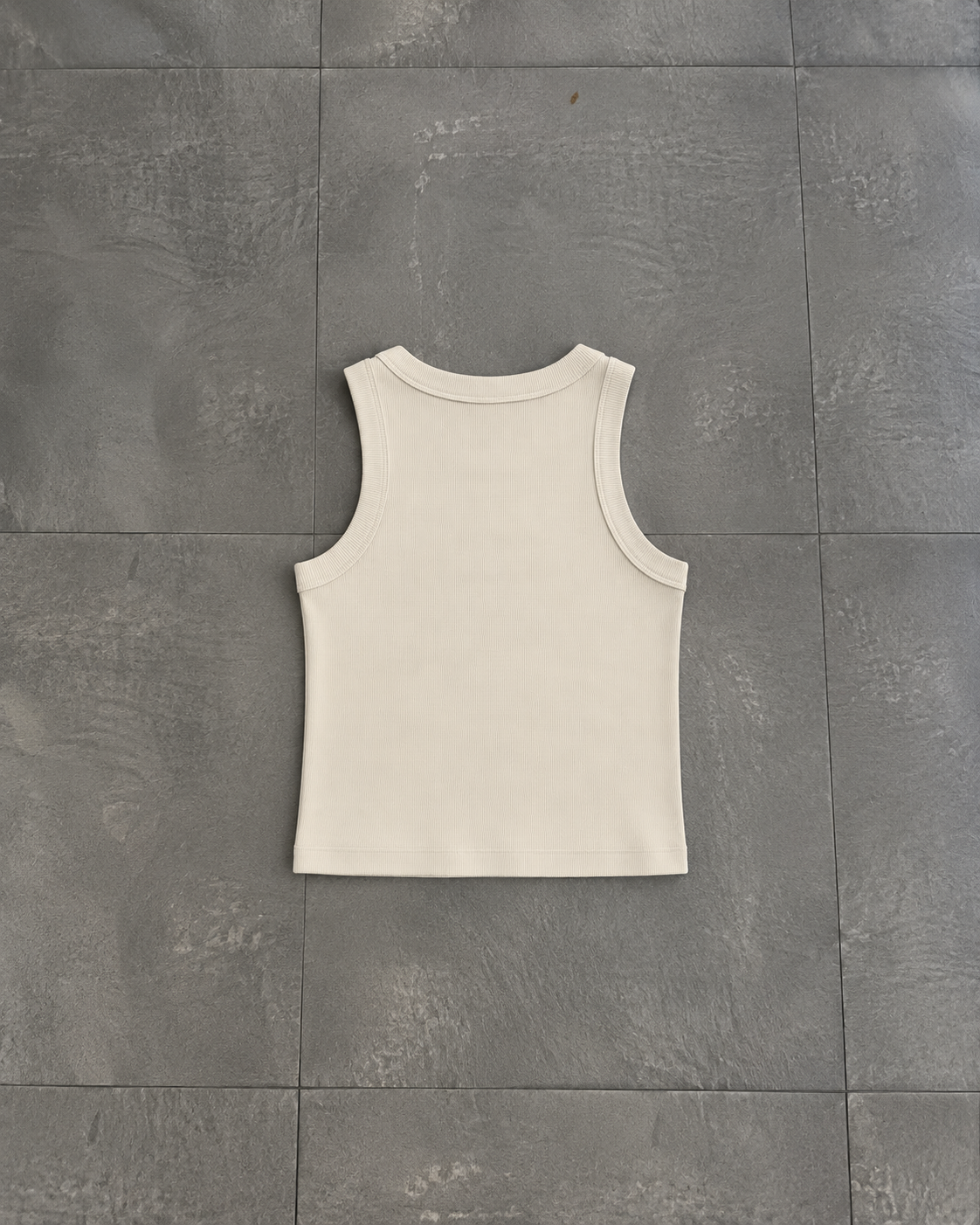 A sleeveless ribbed tank top in off-white, laid flat on a dark gray tiled surface.

Color: Bone Back