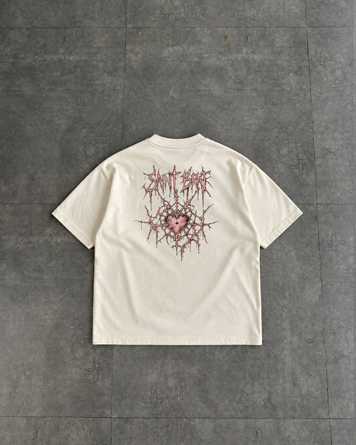 An off-white short-sleeve t-shirt laid flat on a dark gray tiled floor, showing the back of the garment with a graphic print of a thorny heart and stylized text in red and pink.

Color: Vintage White Back