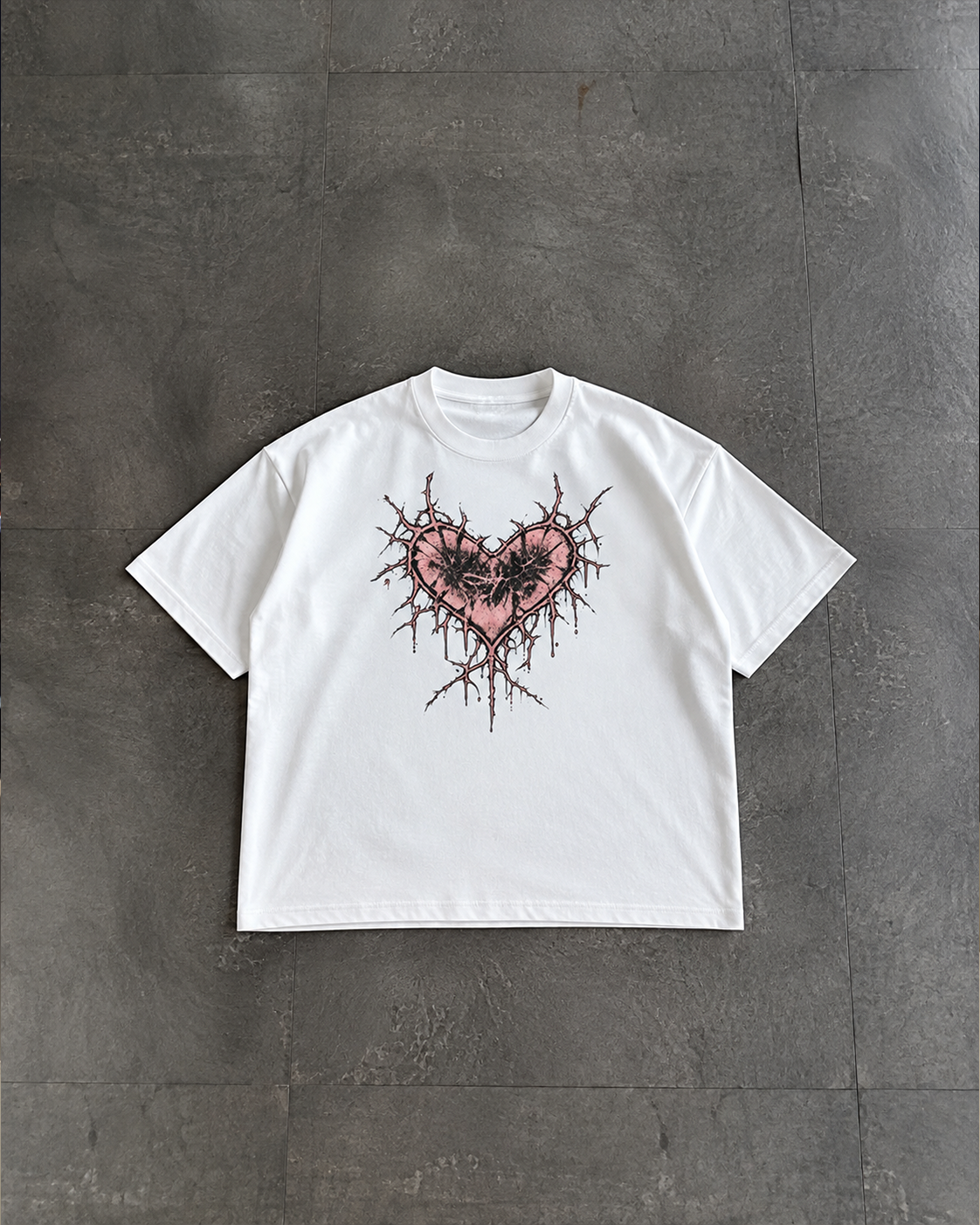 A white short-sleeve crewneck t-shirt featuring a graphic of a pink heart pierced by barbed wire, laid flat on a dark gray textured concrete surface.

Color: White Front