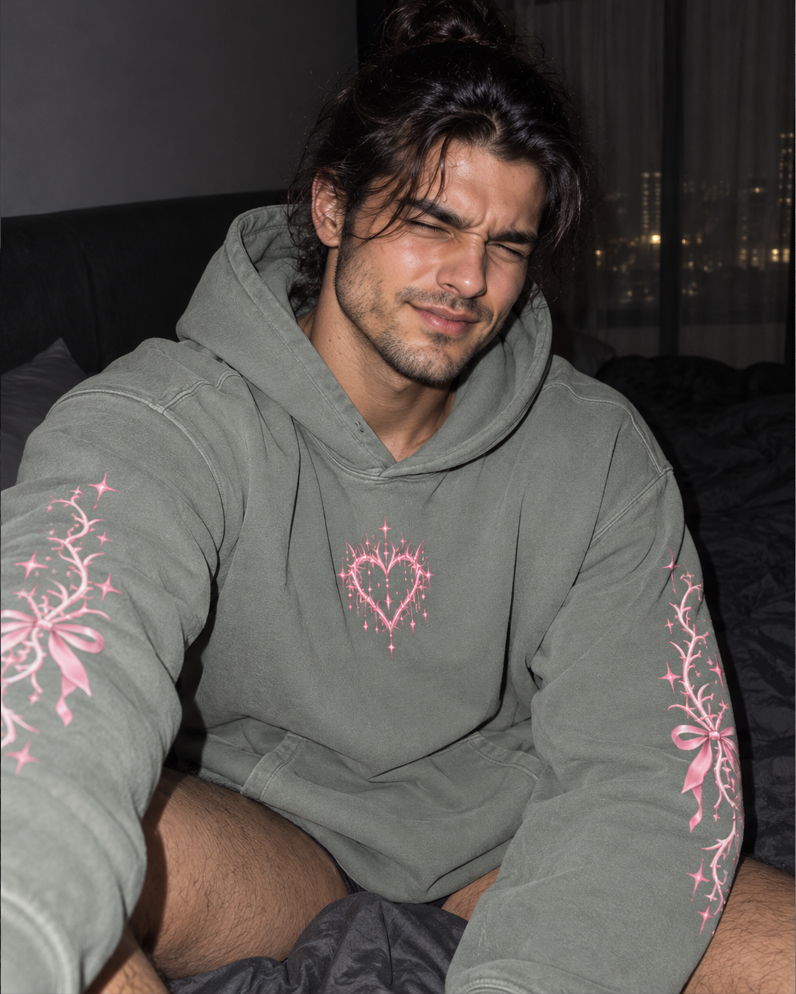 A man wearing an oversized sage green hoodie with pink floral embroidery on the sleeves and a pink heart design on the chest, taking a selfie in a dimly lit bedroom.

Color: Dyed Misty Grey Front