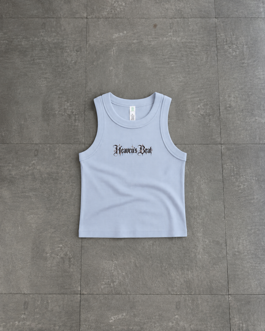 A light blue sleeveless crop tank top with 'Heaven's Rest' printed in a black gothic font across the chest, laid flat on a gray tiled floor.

Color: Powder Front