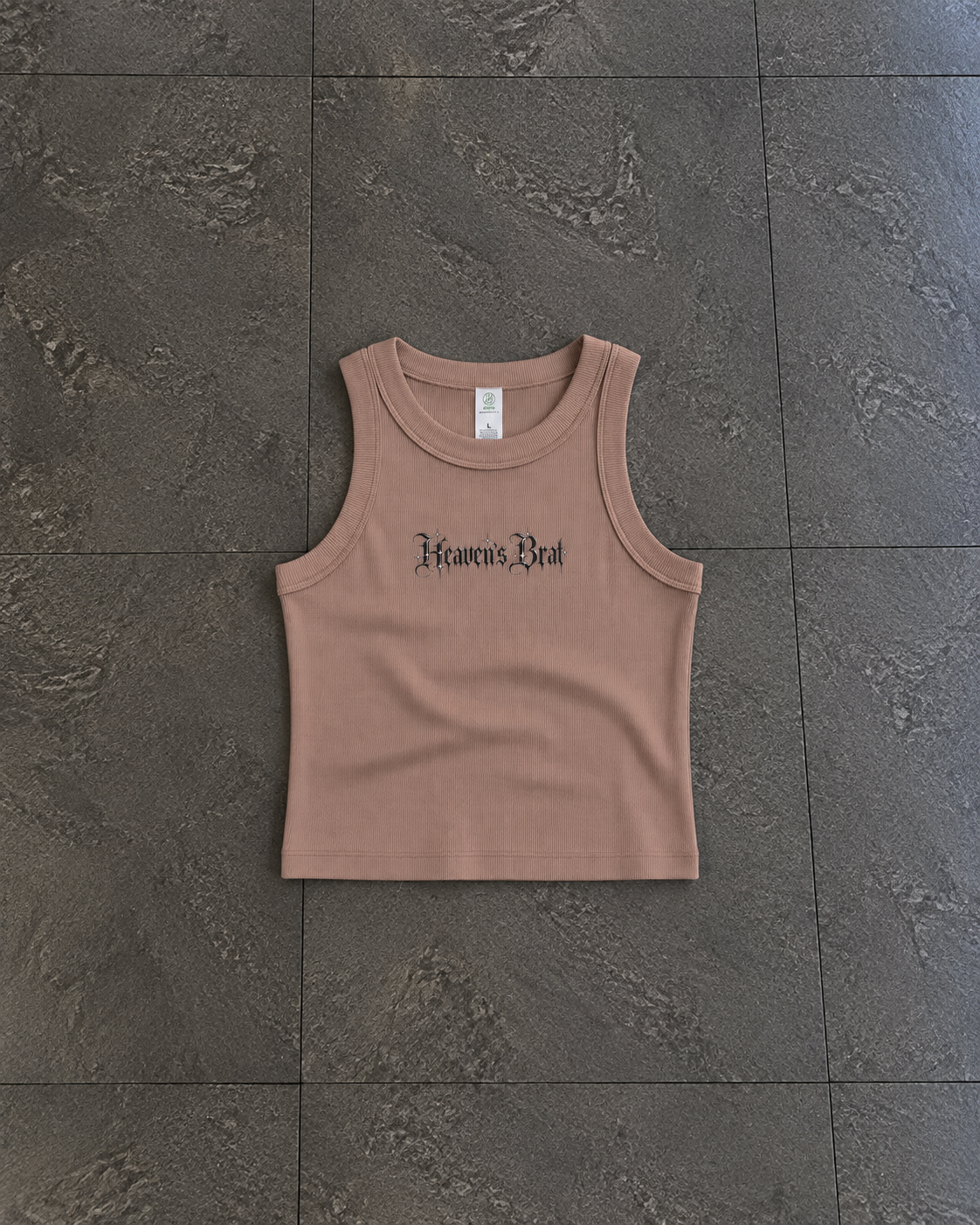 A sleeveless cropped tank top in a muted dusty rose or mauve color, laid flat on a dark gray tiled floor. The front features the text 'Heaven's Rest' in a black gothic font.

Color: Hazy Pink Front