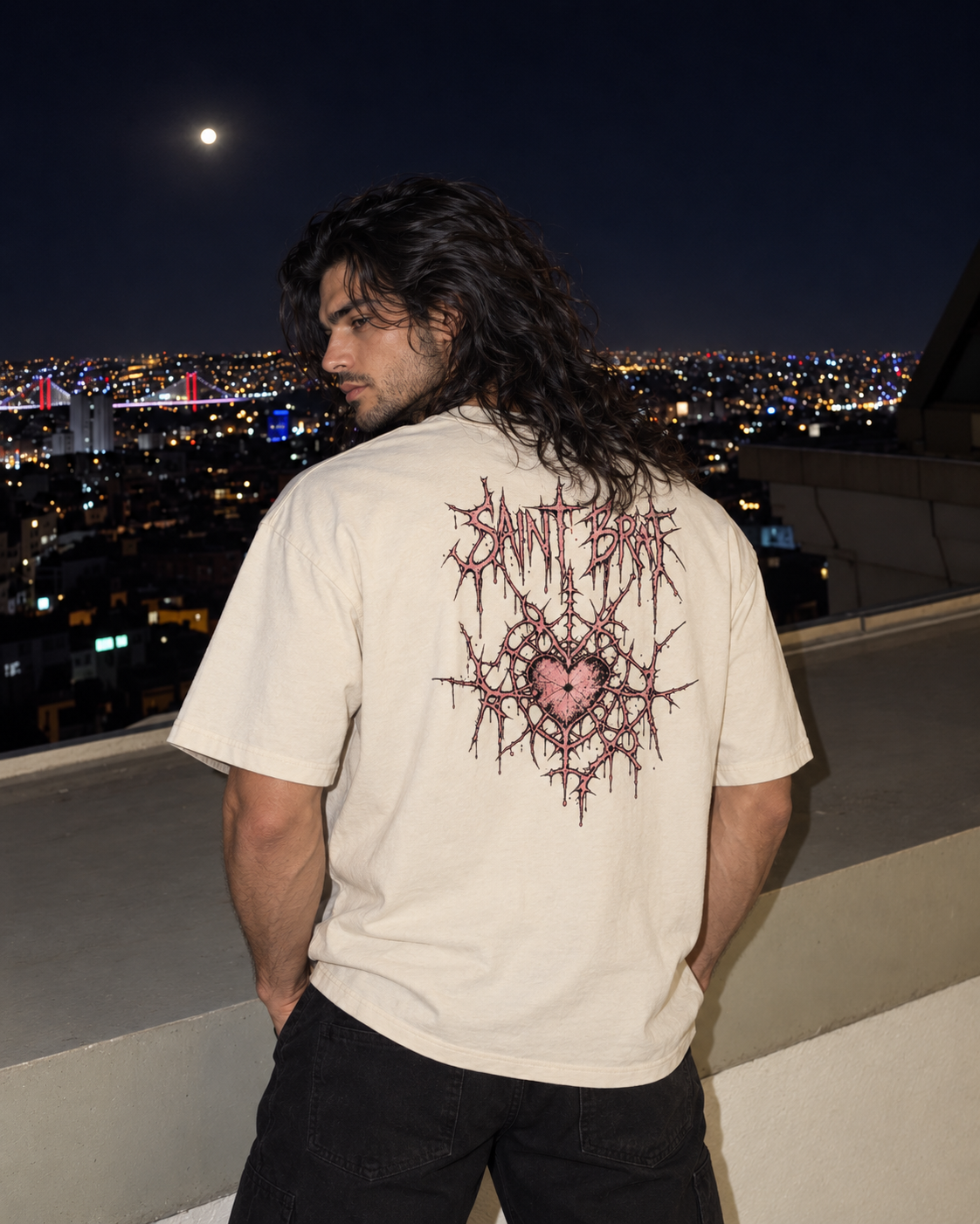 A man with long dark hair stands on a rooftop at night wearing a cream-colored t-shirt with a large pink and red thorn graphic and the text 'Saint Beckett' on the back, overlooking a city skyline under a full moon.

Color: Vintage White Back
