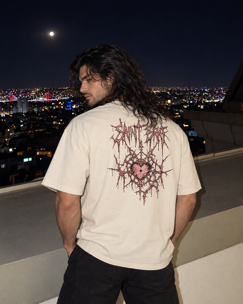 A man with long dark hair stands on a rooftop at night wearing a cream-colored t-shirt with a large pink and red thorn graphic and the text 'Saint Beckett' on the back, overlooking a city skyline under a full moon.

Color: Vintage White Back