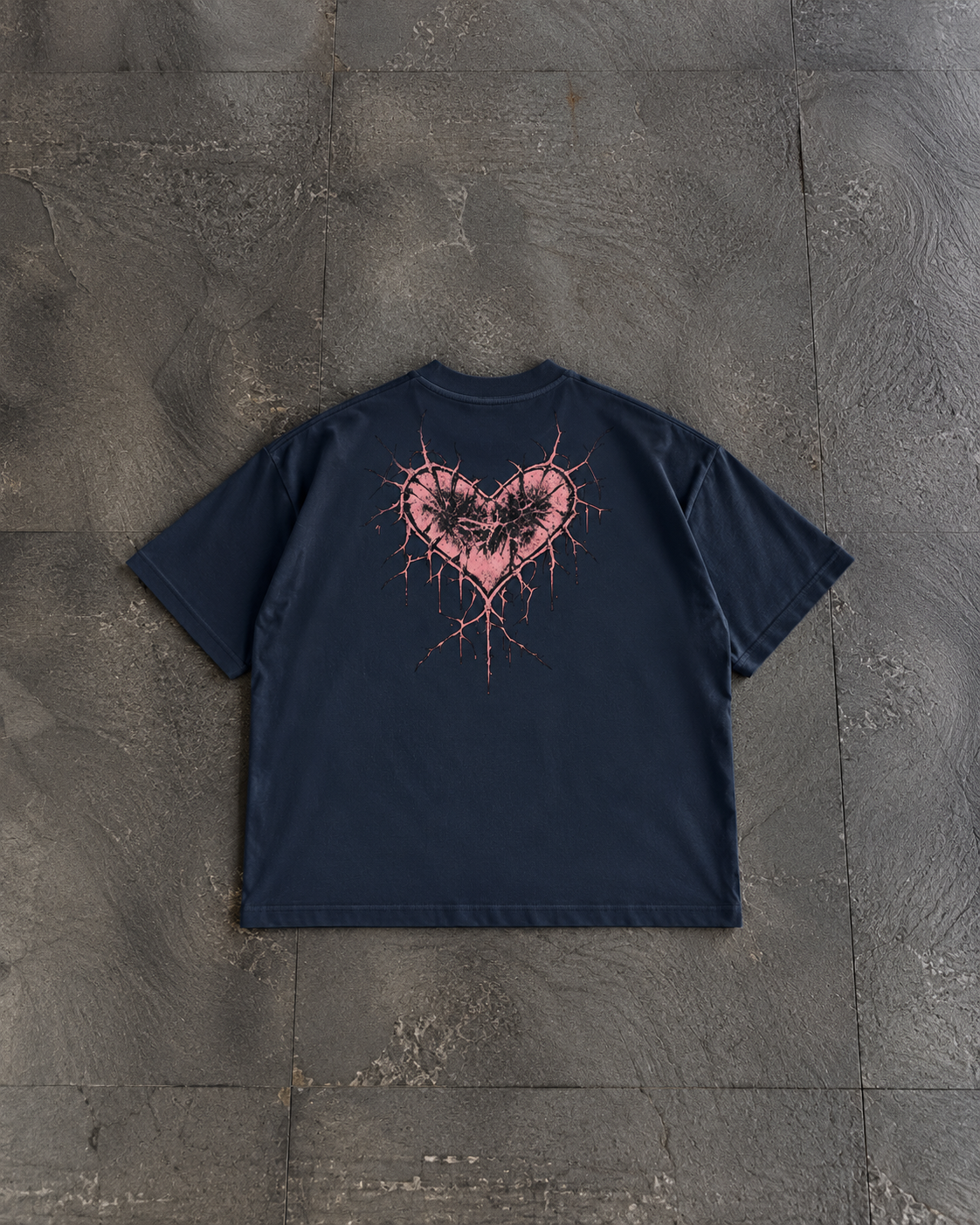 A navy blue short-sleeve t-shirt laid flat on a textured gray concrete surface, featuring a distressed pink and black heart graphic on the back.

Color: Navy Blazer Front