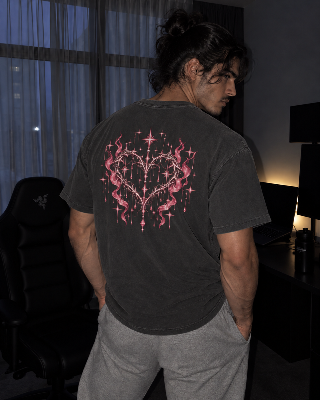 A man wearing a faded black graphic t-shirt with a pink heart-shaped flame design on the back, standing in a dimly lit room.

Color: Pepper Back 