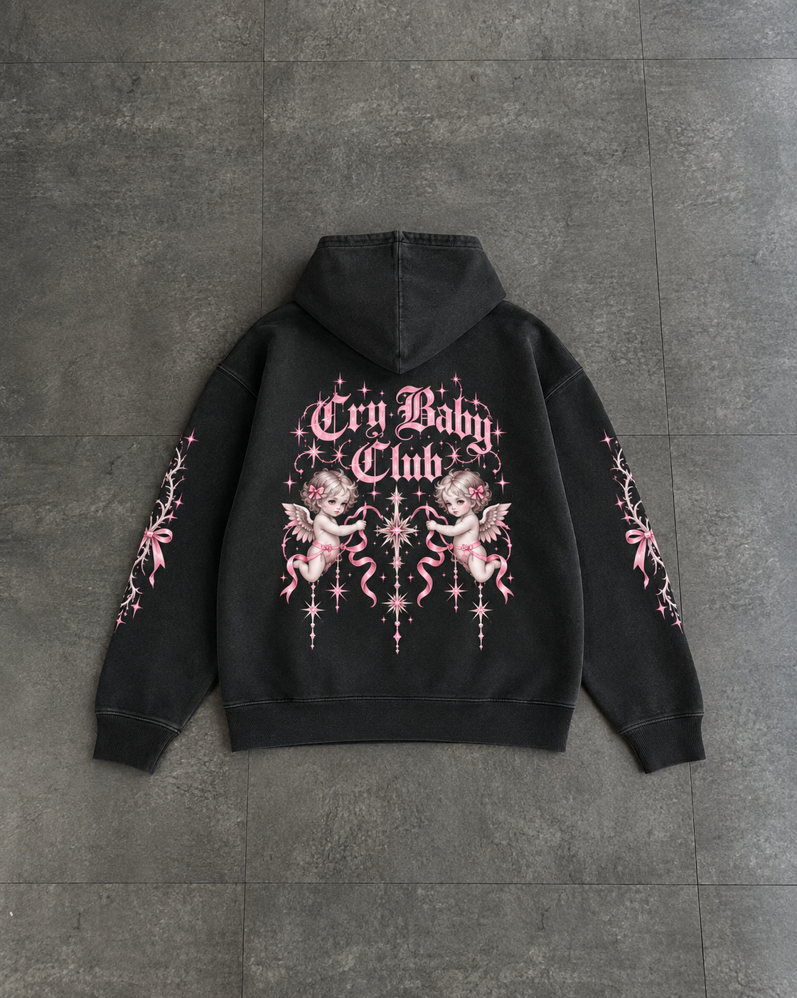 A black pullover hoodie laid flat on a dark gray tiled surface, showing the back view with a large pink and white graphic print that reads 'Cry Baby Club' with cherub illustrations and sleeve prints.

Color: Dyed Black Rock Back