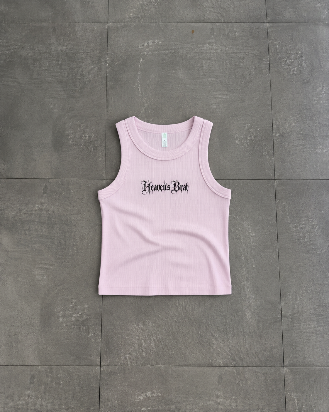 A light pink sleeveless crop tank top with 'Heaven's Bent' printed in a black gothic font across the chest, laid flat on a gray tiled floor.

Color: Orchid Front