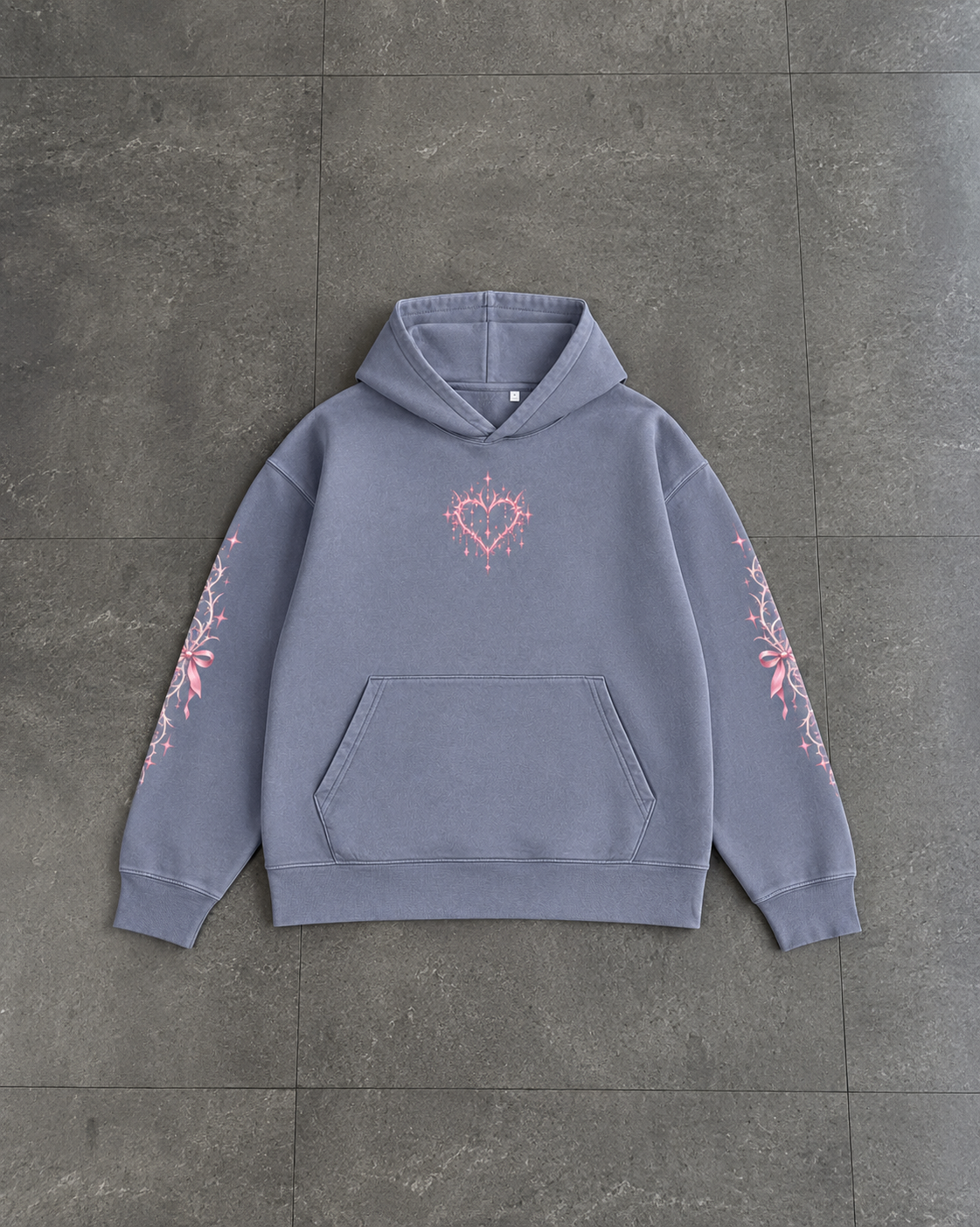 A slate blue-gray pullover hoodie with a pink heart and floral graphic on the chest and sleeves, laid flat on a dark gray tiled floor.

Color: Dyed Blue Grey Front