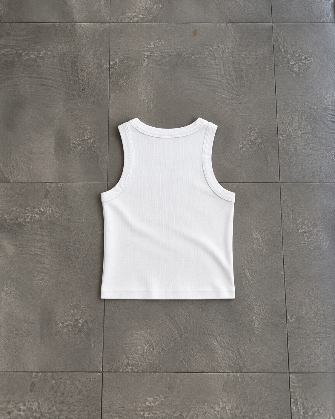 A plain white sleeveless tank top laid flat on a dark gray tiled floor.

Color: White Back